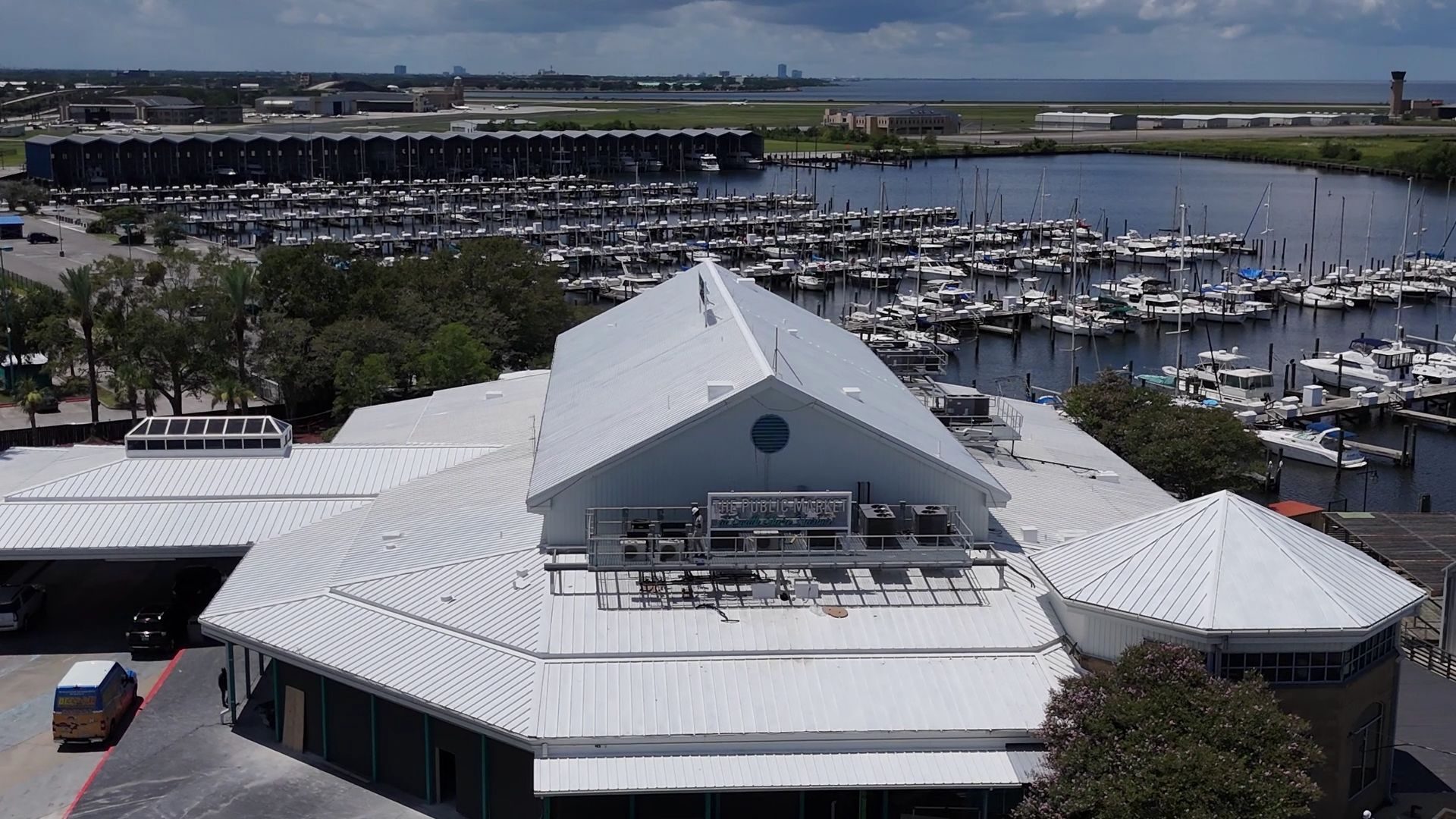 Aerial view of the market's white metal roof and Public Market sign, with the marina and the lake beyond.